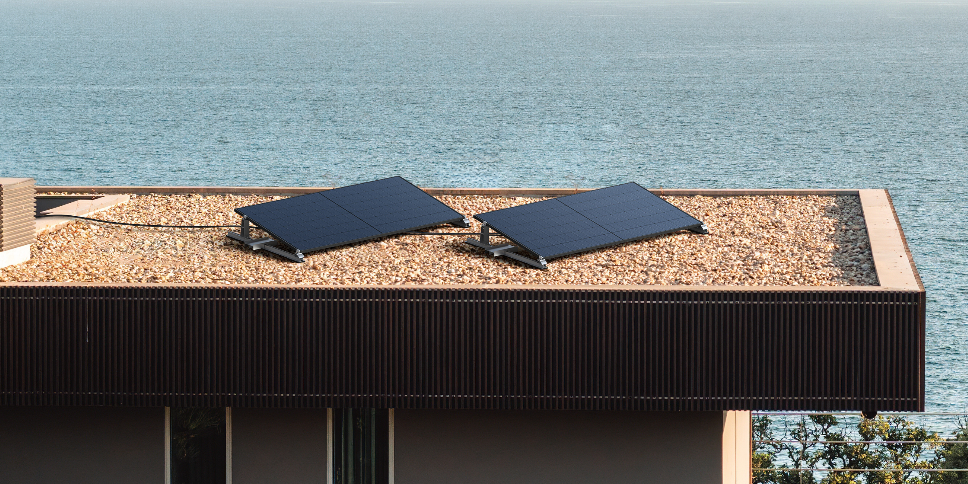 Auf einem Flachdach stehen zwei Solarmodule. Im Hintergrund ist das Meer zu sehen.